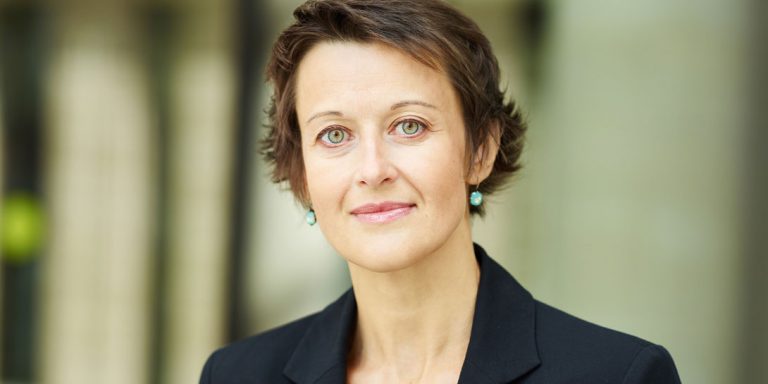 En kvinde i sort jakkesæt og med grønne øreringe