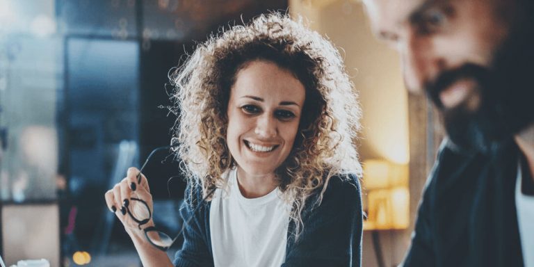 En kvinde med krøllet hår og et par briller i hånden