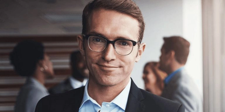 En mand i jakkesæt og med briller står foran en gruppe mennesker