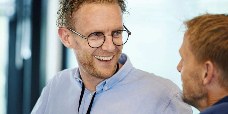 En mand med briller snakker med en anden mand